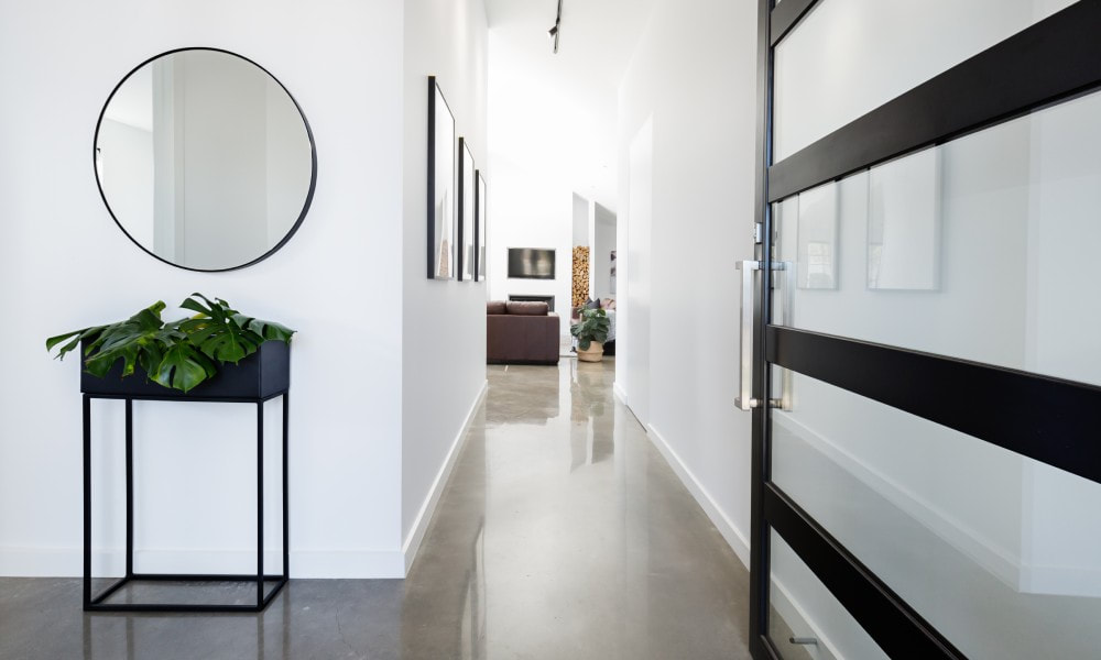 The entryway of a contemporary home, minimally decorated with a standing planter and a round mirror.